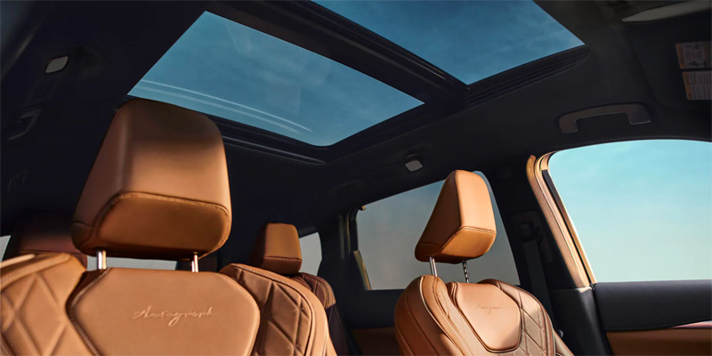 2025 INFINITI QX60 brown leather car seats with a panoramic sunroof showing a blue sky.