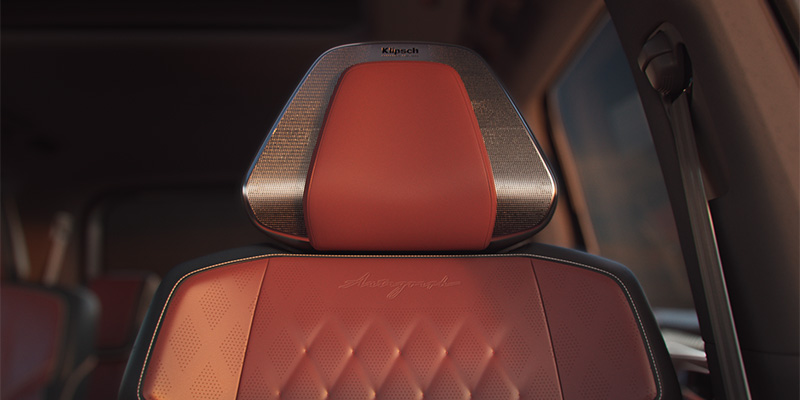 Close-up of a red leather 2025 INFINITI QX80 seat with a stylish headrest featuring Klipsch logo.