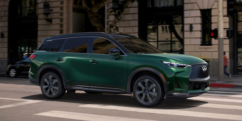 2026 INFINITI QX60 Sport SUV driving through a city street in Grapevine, TX, featuring a bold grille, sleek lines, and modern luxury styling.