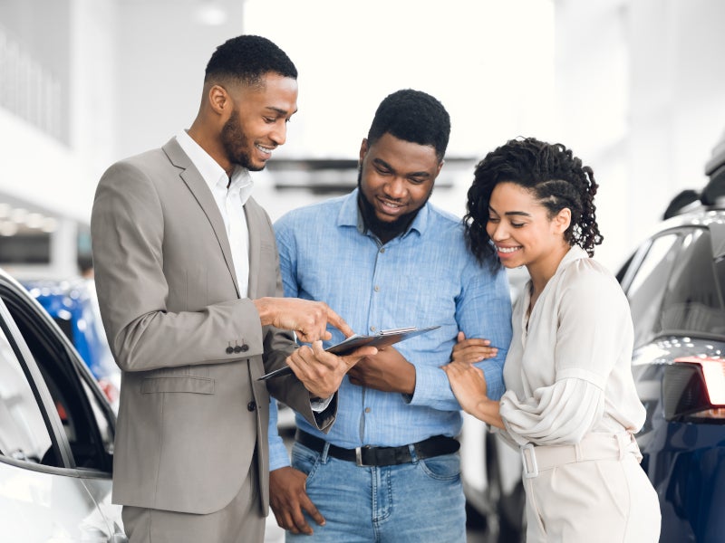 Two Salesmen and a sales woman at a dealership smiling